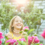 happy little girl with braces in the garden in bushes of peonies